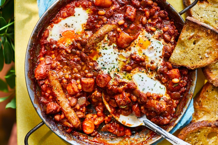 Wide pan of smoky beans, chorizo and egg stew with cup of tea