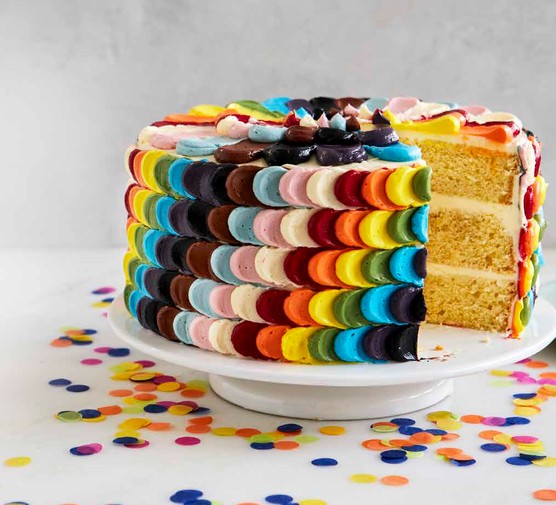 A cake with multiple coloured icing sits on a cake stand surrounded by confetti