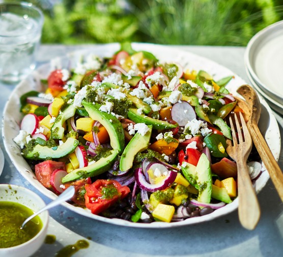 Plate of colourful summer salad topped with halloumi, with cutlery