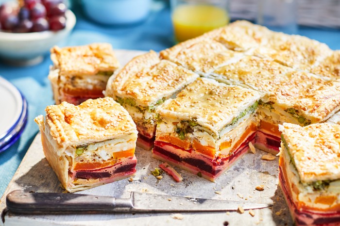 Vegetarian layered pie sliced into squares on a serving board