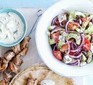 Greek salad in a bowl alongside kebabs and tzatziki