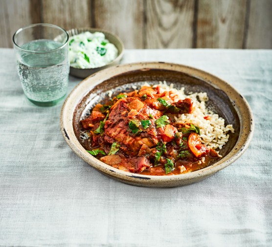 Bowl of chicken curry and rice next to a bowl of yoghurt and glass of water